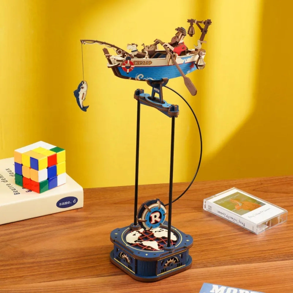 Toy boat on a stand with a Rubik's Cube and cassette tape in the background on a wooden surface.