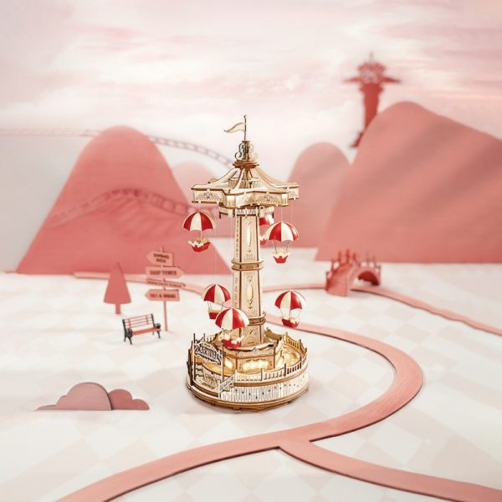 Decorative model of a carousel with red and white striped umbrellas on a pink and white background.