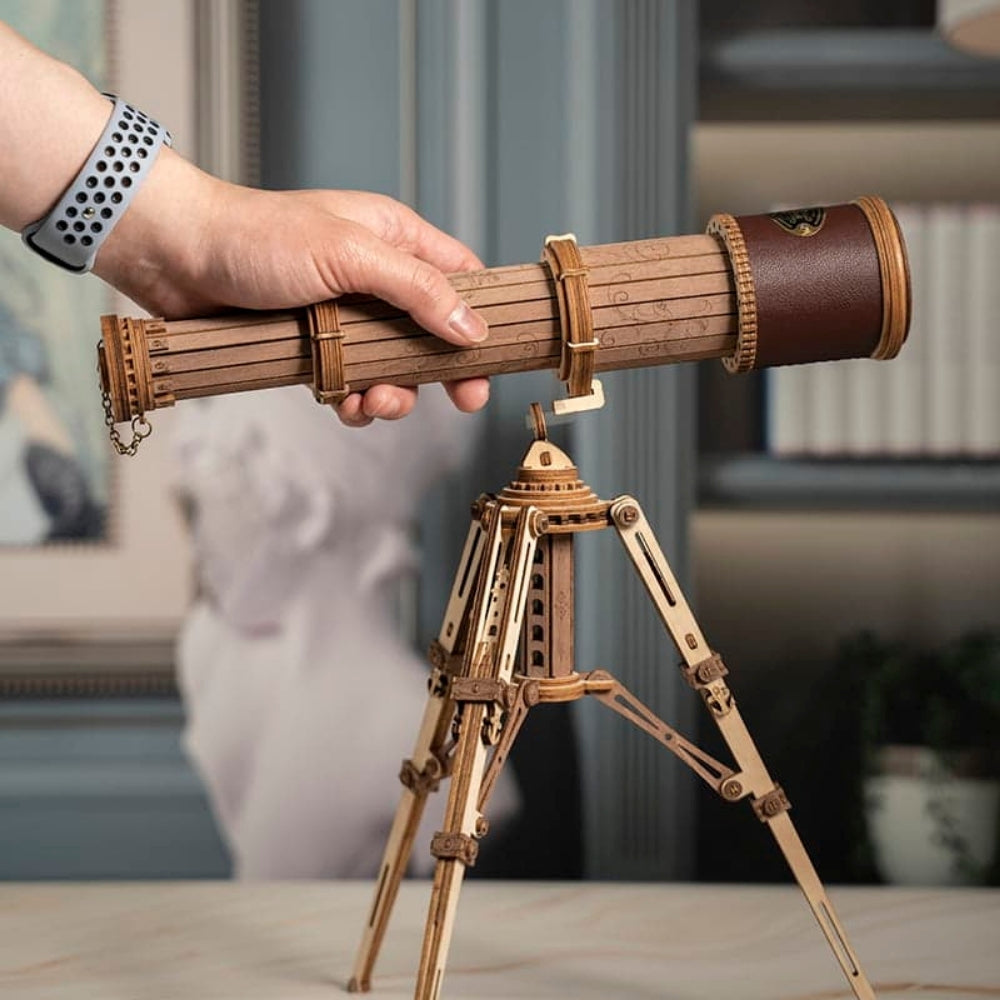 Wooden telescope model on a stand held by a hand with a blurred indoor background