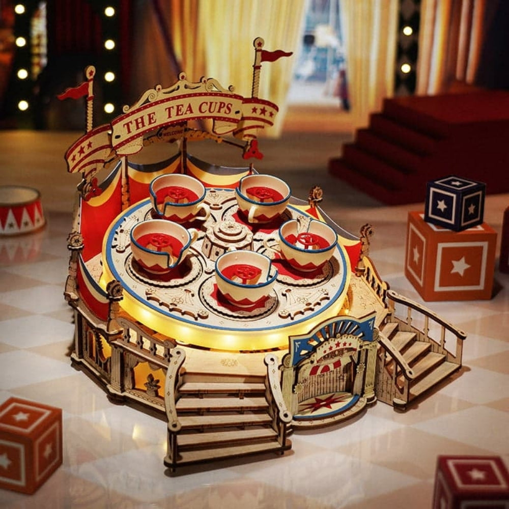 Wooden toy carousel with 'The Tea Cups' sign on a checkered floor.