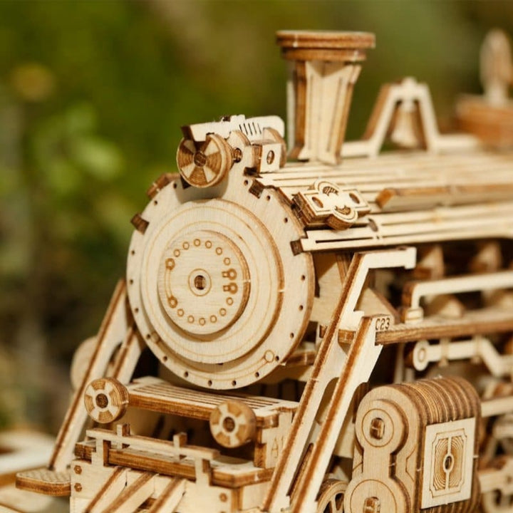 Wooden model of a steam locomotive with intricate details against a blurred natural background